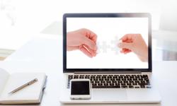 Ordenador portátil en cuya pantalla aparecen dos manos encajando dos piezas de puzzle